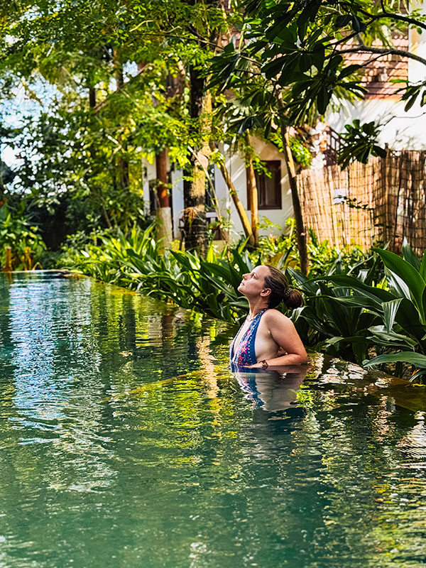 Katie relaxing at the edge of swimming pool in the garden of Dontrei Villa Angkor hotel in Siem Reap