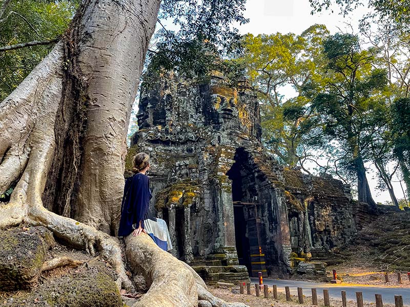 Katie sitting on a tree in front of the North Gate of Angkor Thom, Siem Reap, Cambodia
