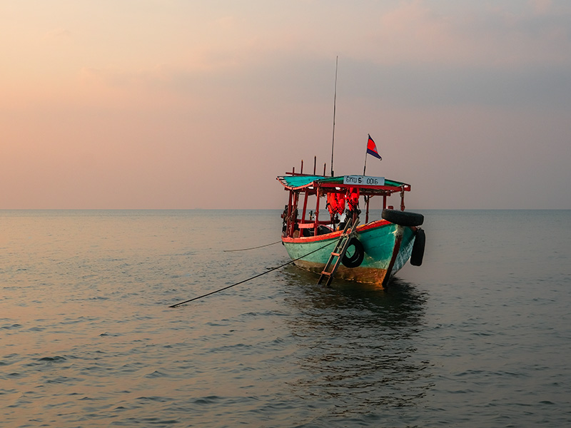 A lone boat in on a calm sea with candy floss coloured sky on the shores on Koh Tonsay, a small Cambodian island