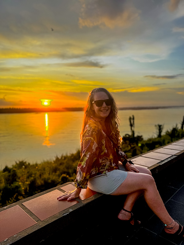 Katie sitting on a wall in Kratie, Cambodia to watch the sunset over the Mekong