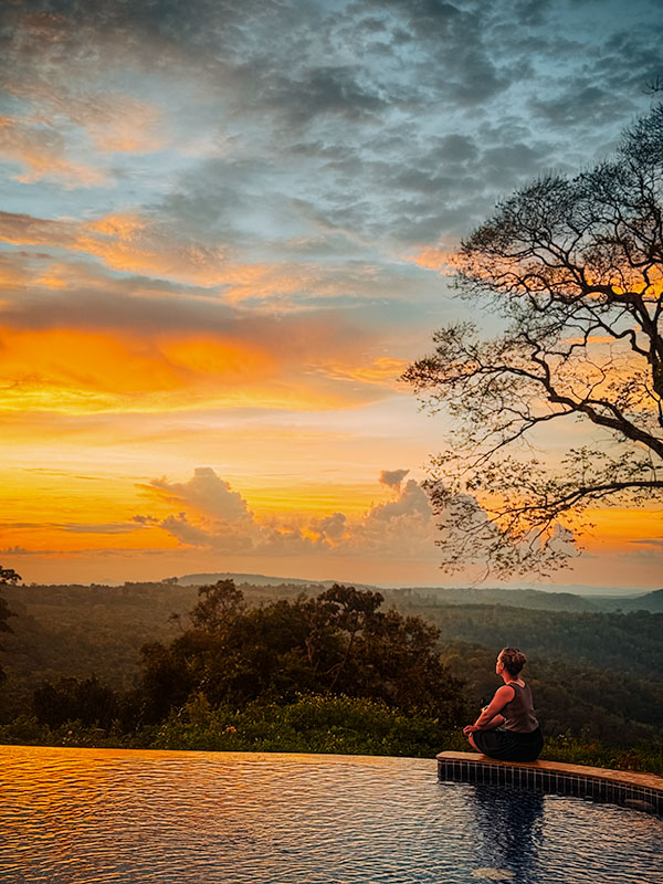 Katie sitting on the edge of the infinity pool at PIDA Coffee Farm watching the sunset over the jungle of Mondolkiri, Cambodia