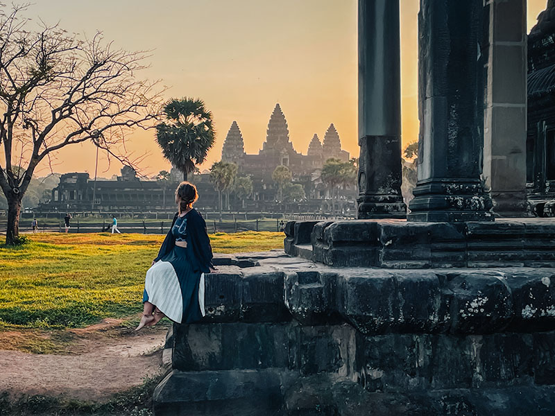 Katie sitting on stone stairs watching the sunrise of Angkor Wat, a bucket list moment in Cambodia
