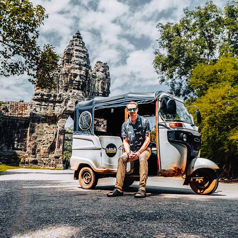 Matt sitting in a tuktuk (with TukTukRental branding) in front of the Tomle Om South Gate at Angkor Archaeological Park