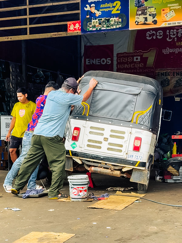 Tuktuk being pushed onto its side to rubber greasing at mechanic shop in Cambodia