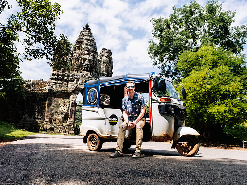 Matt sitting in a rented tuktuk (with Tuktuk Rental branding) in front of Tomle Om in Angkor Thom